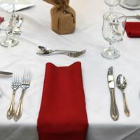 Photo of table place settings with silverware and red napkins on a white tablecloth