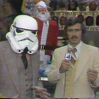 Reporter interviewing man in Star Wars Stormtrooper mask.
