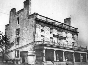 A black and white image of the Frontier House in Lewiston. The building is three stories tall with a large front porch and tall chimneys at both ends of the building.
