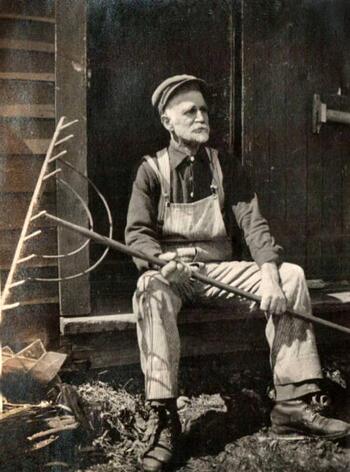 Seated man in overalls holding rake
