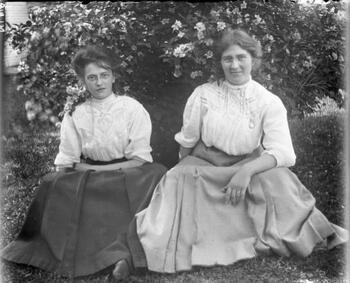 Two women seated near a bush